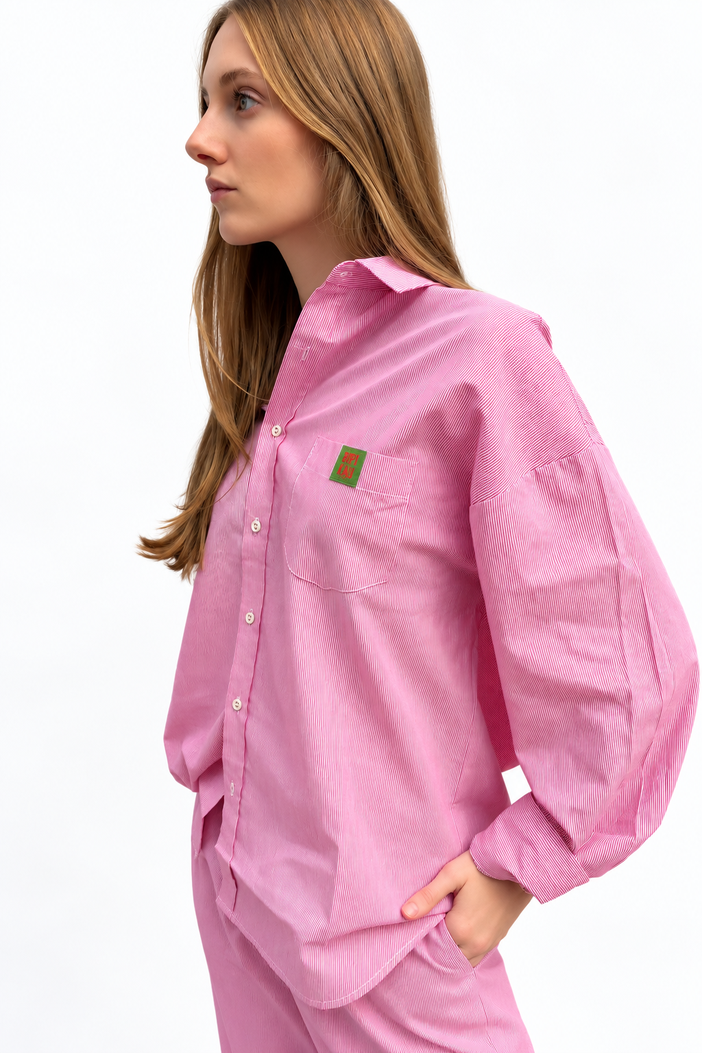 Modelo de perfil con el Soleil Set de Bipikau: camisa oversize rosa de rayas finas con etiqueta en el bolsillo