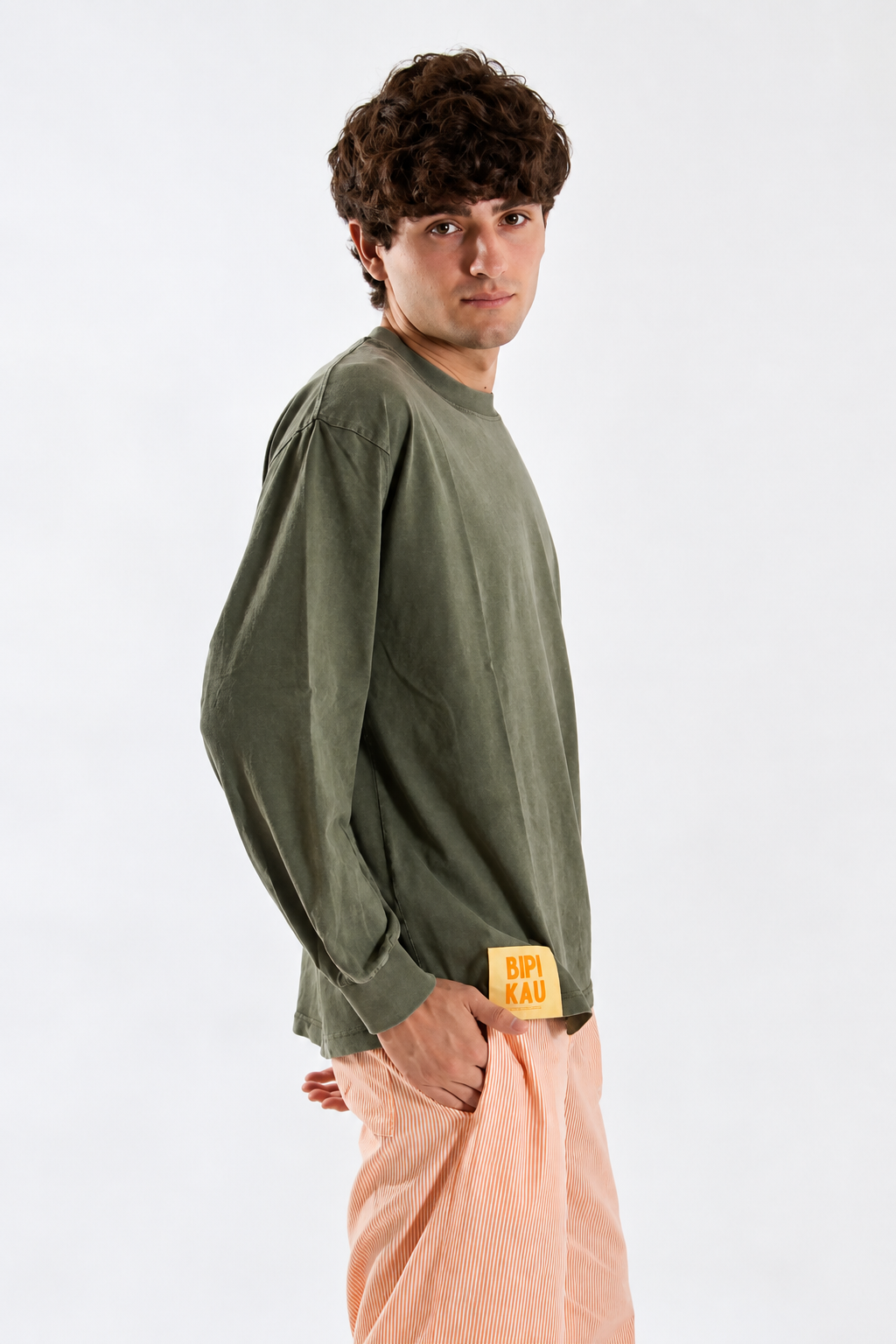 Modelo de perfil con la Cactus Tee Khaki de Bipikau, camiseta oversize verde caqui con etiqueta naranja, y pantalón de rayas